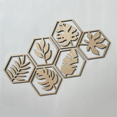 Hexagonal wooden wall art pieces with leaf patterns on a light gray background