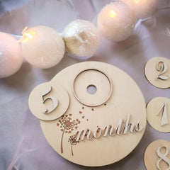 Wooden milestone with '5 months' text, surrounded by decorative lights and beads.