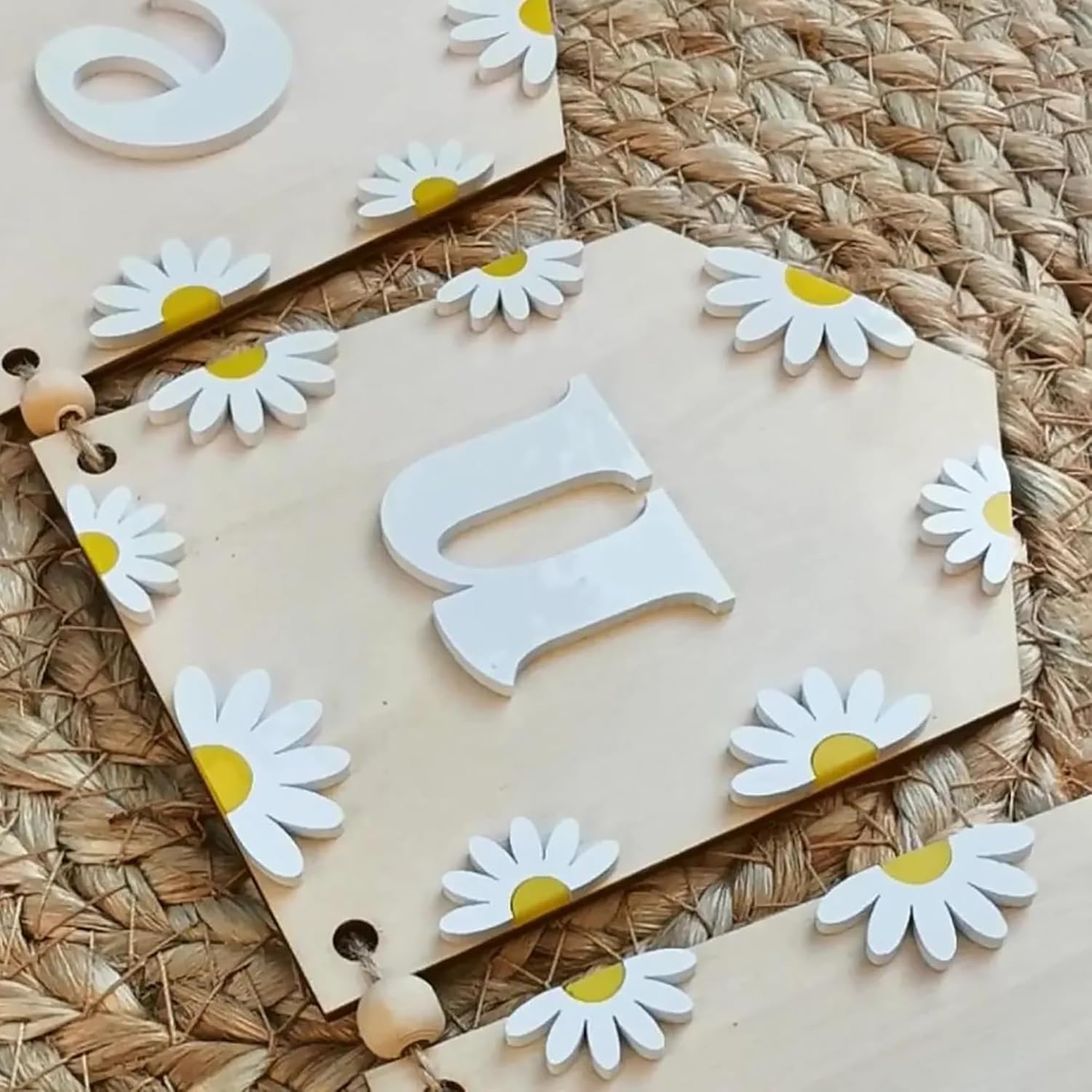 Wooden letters 'Q' and 'P' with daisy flower decorations on a woven mat.