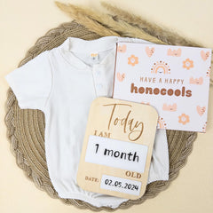 Baby onesie with milestone card and measuring stick on a woven mat