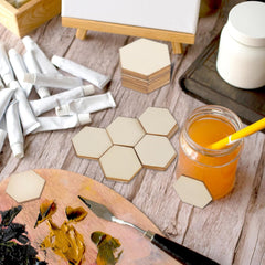 Hexagonal coasters on a wooden surface with art supplies and a drink.