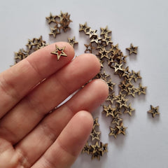Small gold star-shaped earrings on a hand with a light gray background