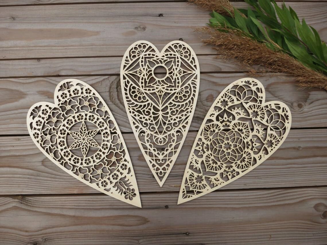 Three ornate heart-shaped wooden decorations on a wooden surface with greenery.
