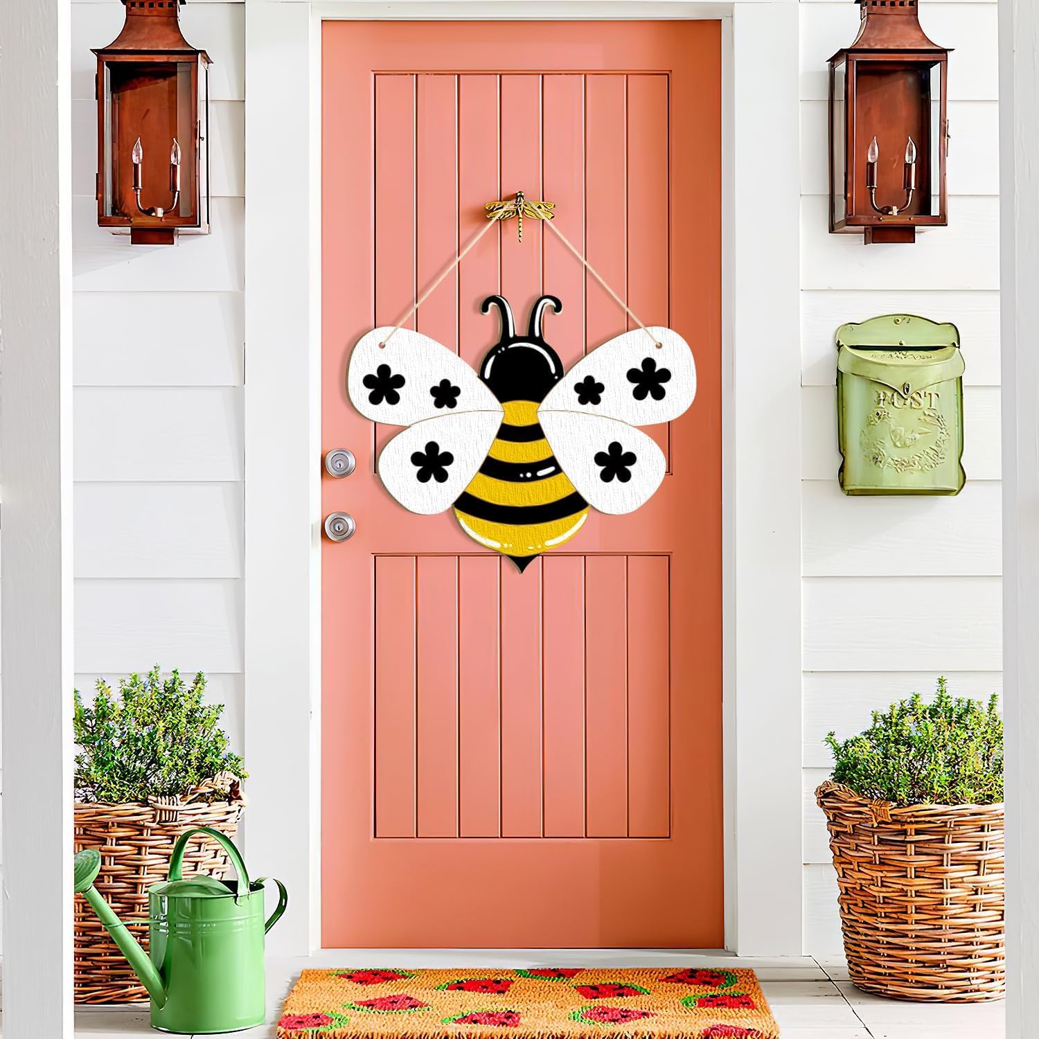 Pink door with a bee-shaped decoration, green watering can, and planters on a white wall.