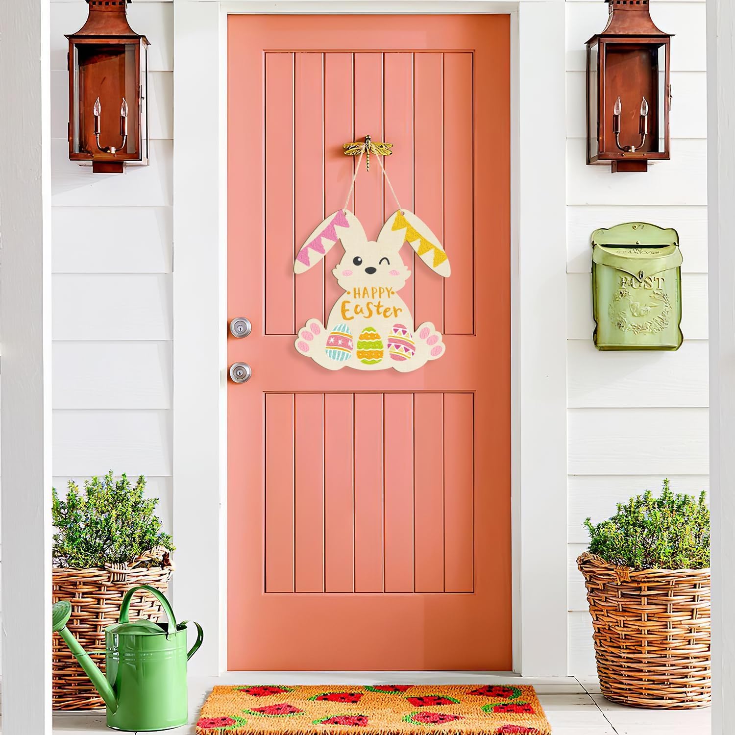 Pink door with Easter decorations, green watering can, and plants on a white wall.