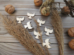 Wooden angel charms on a wooden surface with dried plants and walnuts.