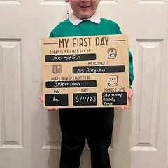 Child holding a 'My First Day' sign in front of a white door