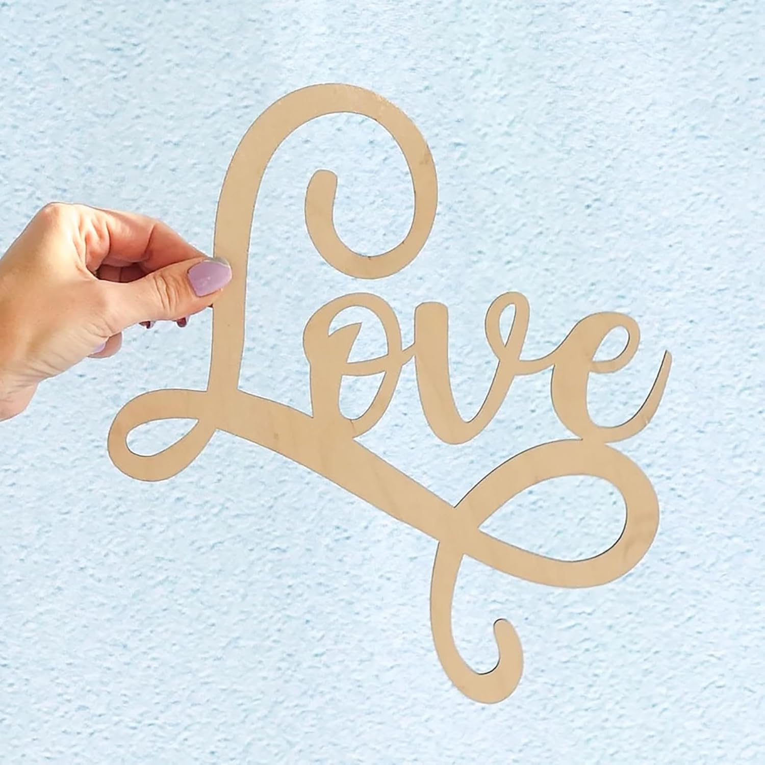 Wooden 'love' sign held by a hand against a light blue background