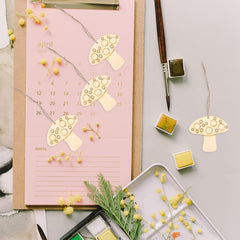 Pink calendar with gold mushroom designs and stationery items on a light gray background