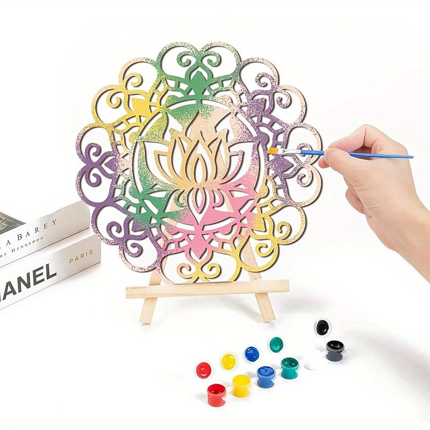 Colorful mandala art set with a hand holding a paintbrush and a small easel on a white background.