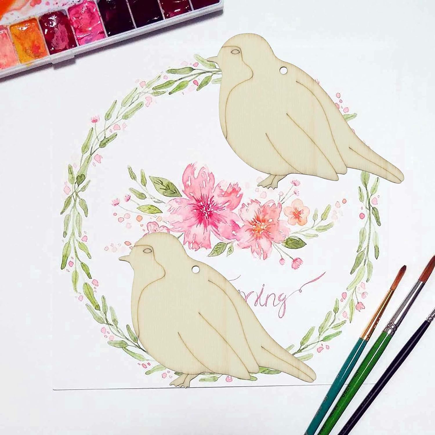 Two doves with flowers and leaves on a white background with watercolor paints and brushes.