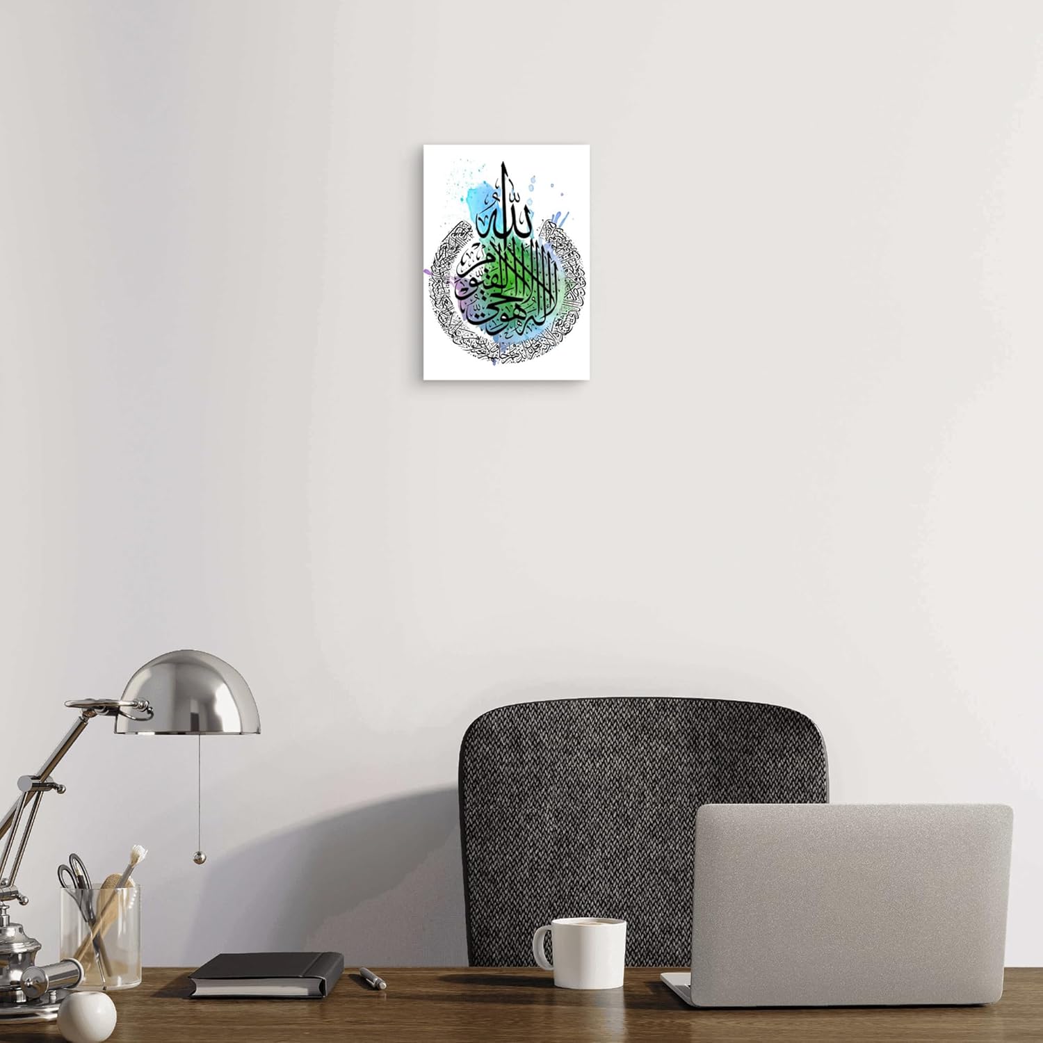 Decorative wall art with Arabic calligraphy on a white wall above a desk with a laptop and lamp.