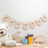 Wooden dinosaur banner on a wall with a teddy bear and stationery items below.