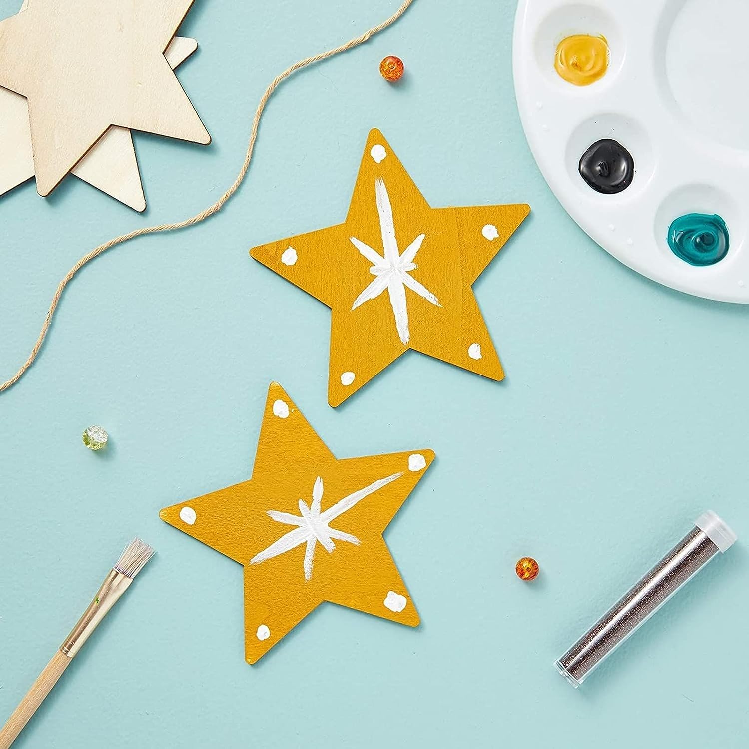 Two yellow star-shaped decorations with white centers on a light blue background, surrounded by craft supplies.