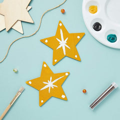 Two yellow star-shaped decorations with white centers on a light blue background, surrounded by craft supplies.