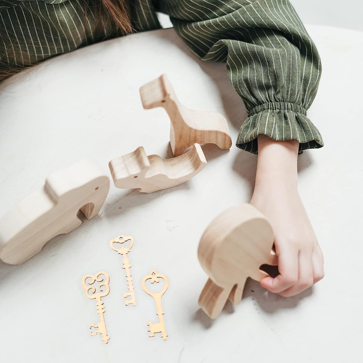 Wooden toys and keys on a light surface with a person's arm in green striped sleeves.
