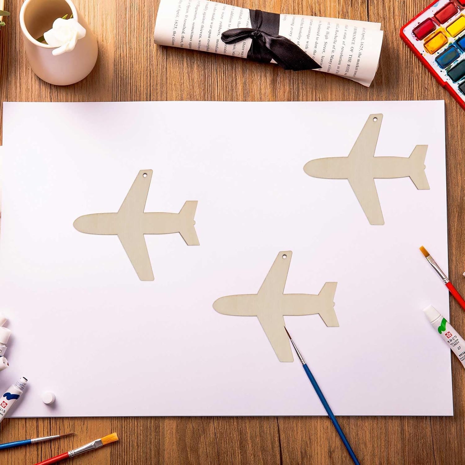 Three airplane shapes on a piece of paper with art supplies on a wooden table.
