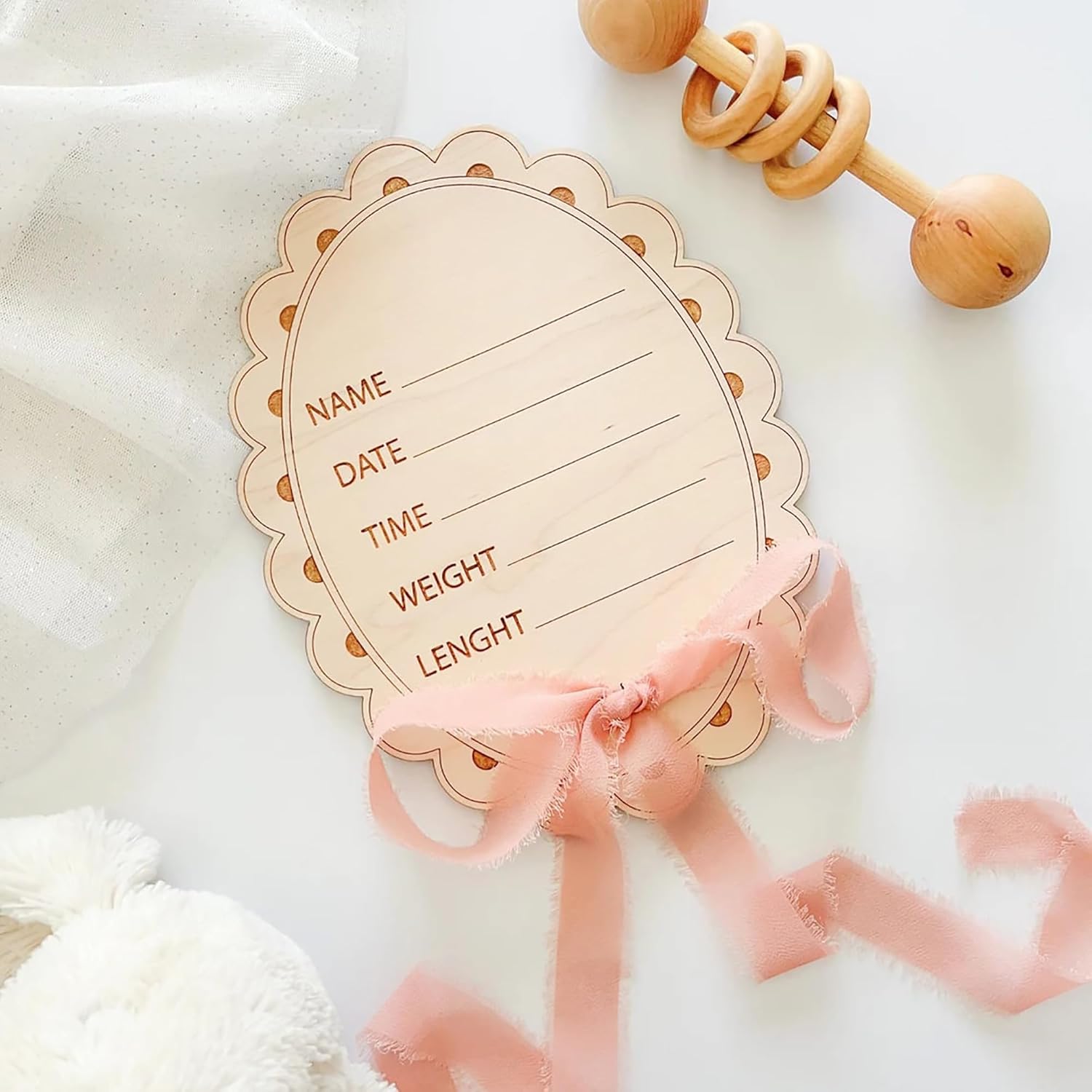 Wooden baby milestone card with decorative ribbon and wooden teething toy on a soft white background