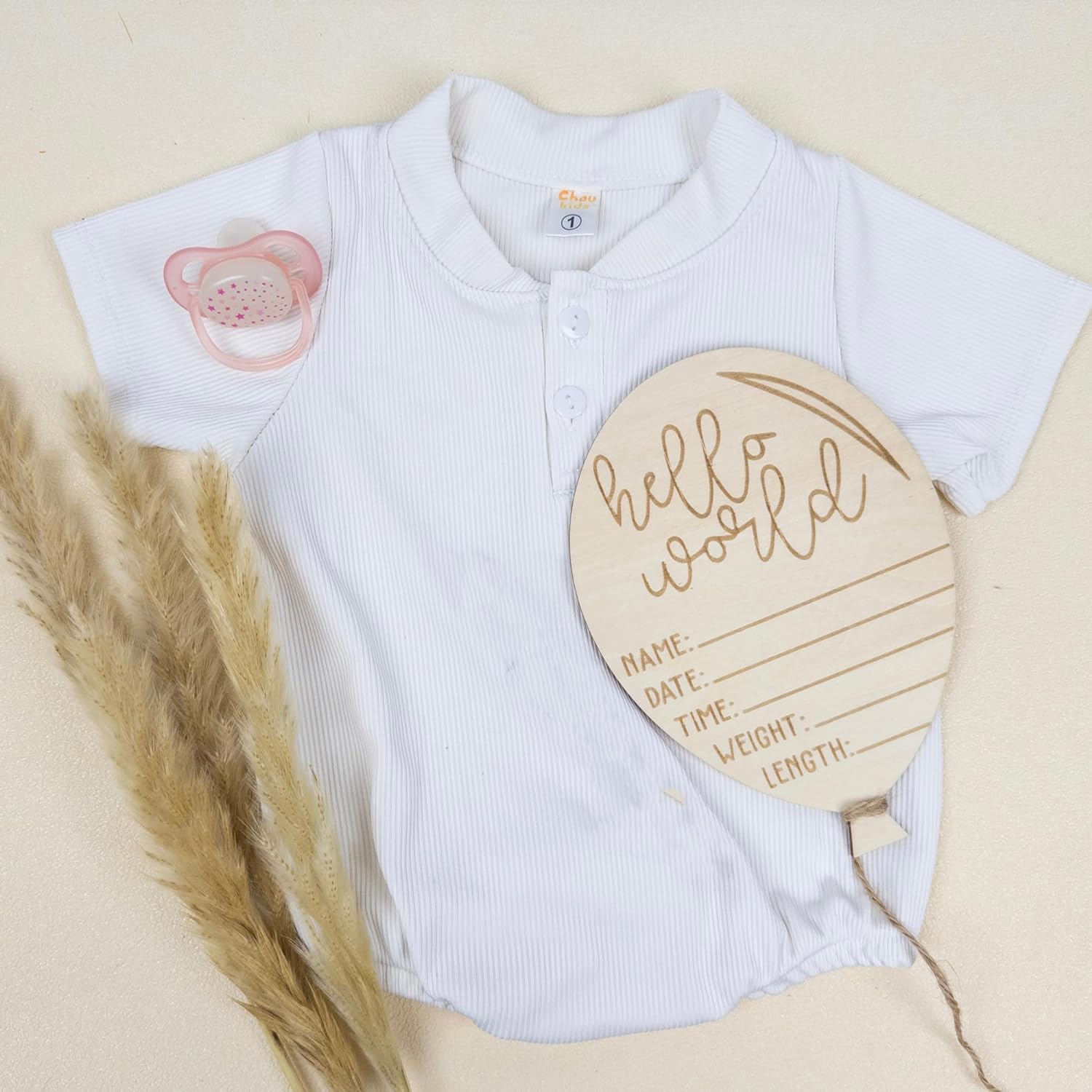 White baby onesie with a pacifier design and a wooden plaque on a beige background