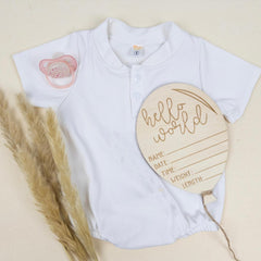 White baby onesie with a pacifier design and a wooden plaque on a beige background