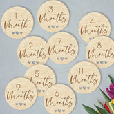 Wooden milestone discs for baby photoshoots with months printed on them against a light blue background.