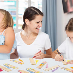 Woman and two children sitting at a table with coloring books and crayons, smiling and engaged in an activity.