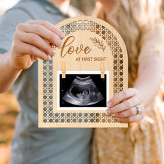 Wooden frame with 'Love at First Sight' text holding an ultrasound photo, held by a person.