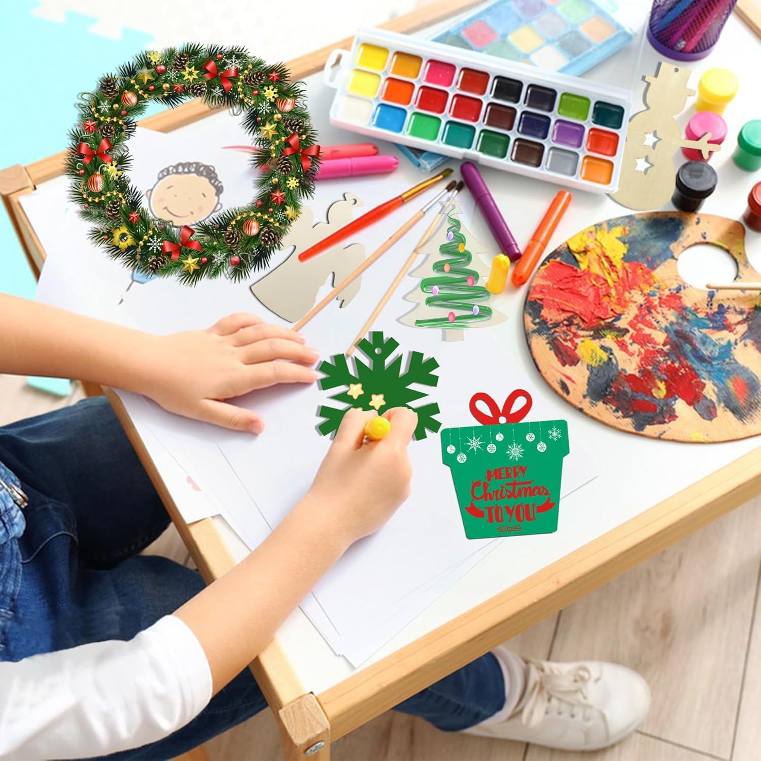 Children's hands working on Christmas-themed crafts with art supplies on a table.