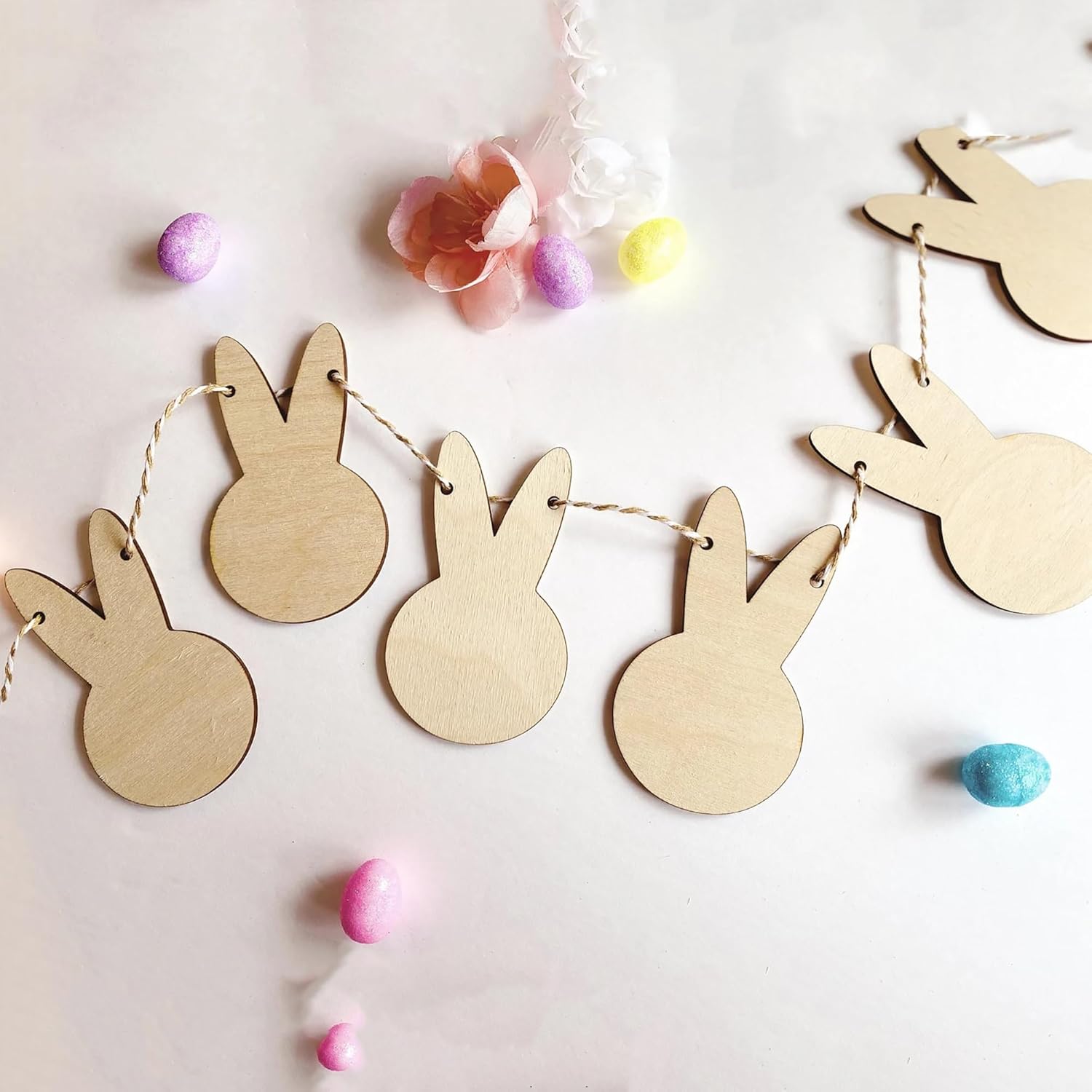 Wooden bunny-shaped decorations on a string with Easter eggs and flowers on a light background