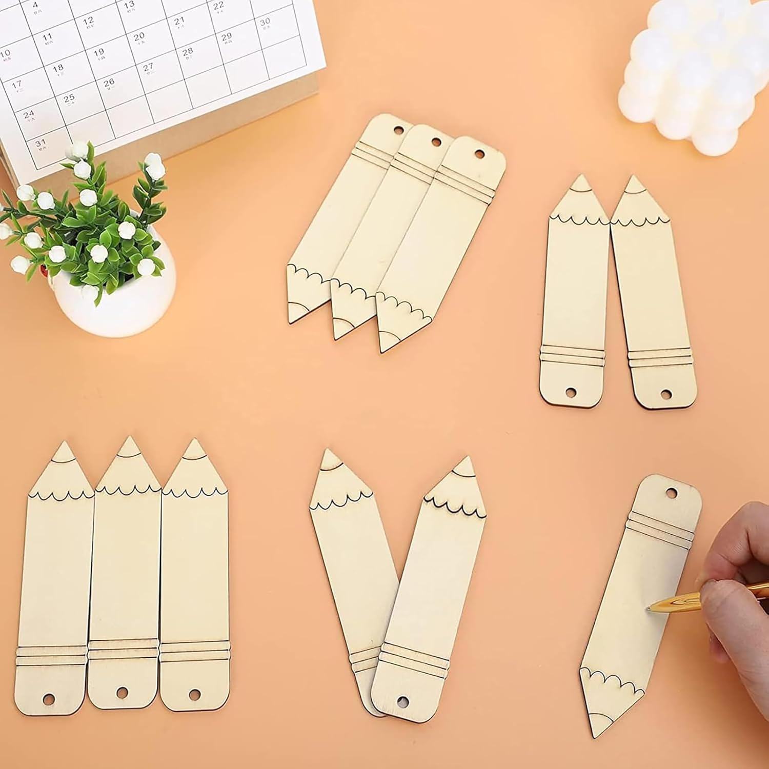 Wooden pencil-shaped bookmarks on a peach-colored surface with a hand holding a pencil.