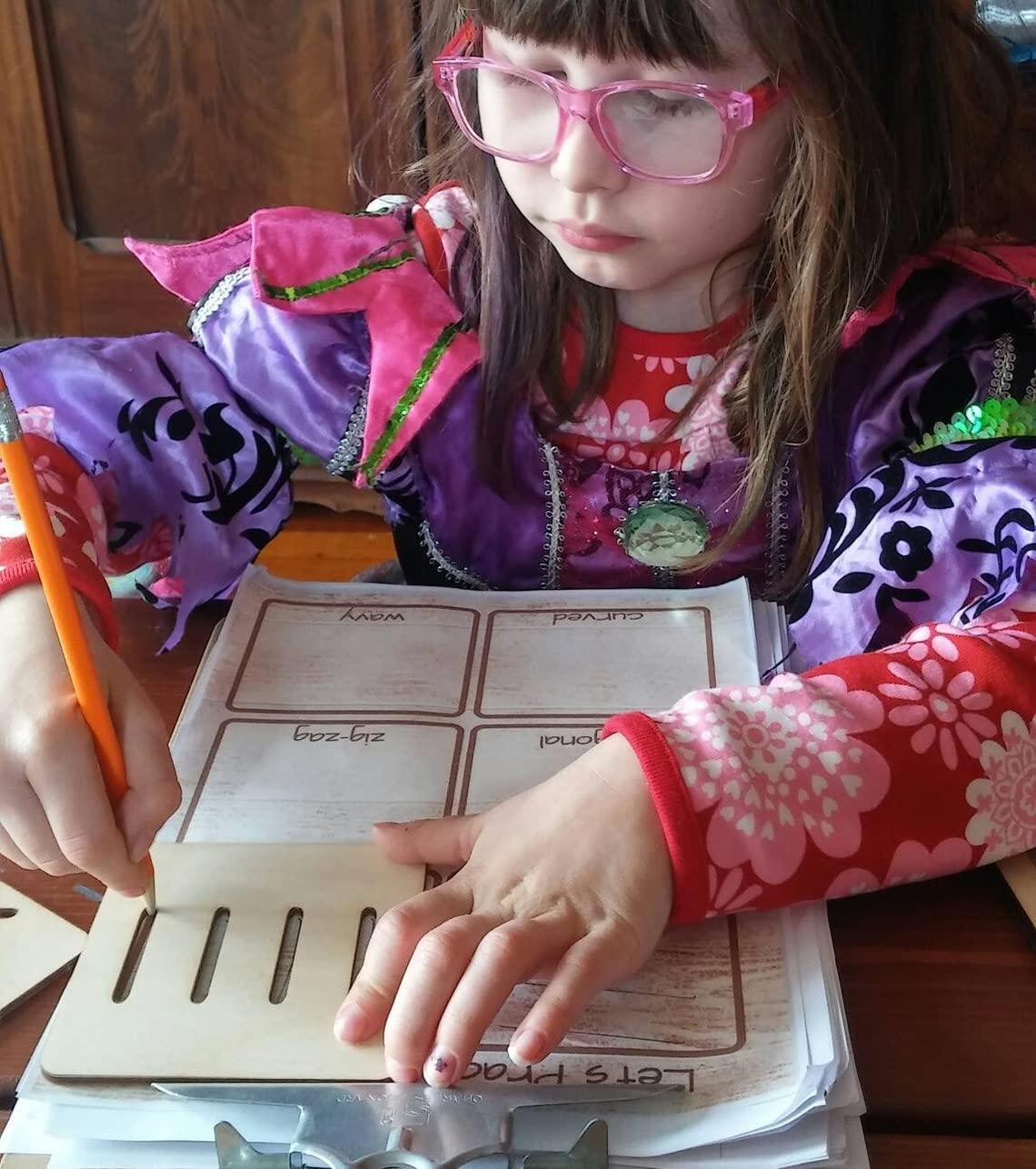 Child wearing glasses and a colorful jacket, engaged in writing or drawing on a piece of paper.