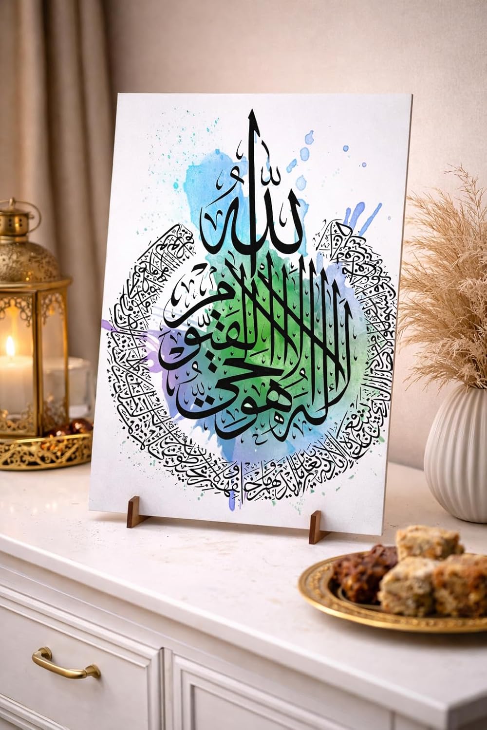 Decorative piece with Arabic calligraphy on a stand, placed on a surface with a candle and snacks.