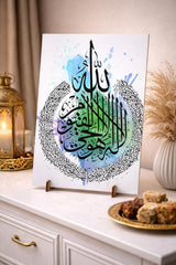 Decorative piece with Arabic calligraphy on a stand, placed on a surface with a candle and snacks.