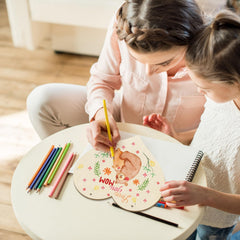 Two children drawing on a round wooden board with colorful pencils.