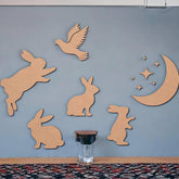 Wooden cutouts of rabbits, a bird, and a moon with stars on a blue wall.