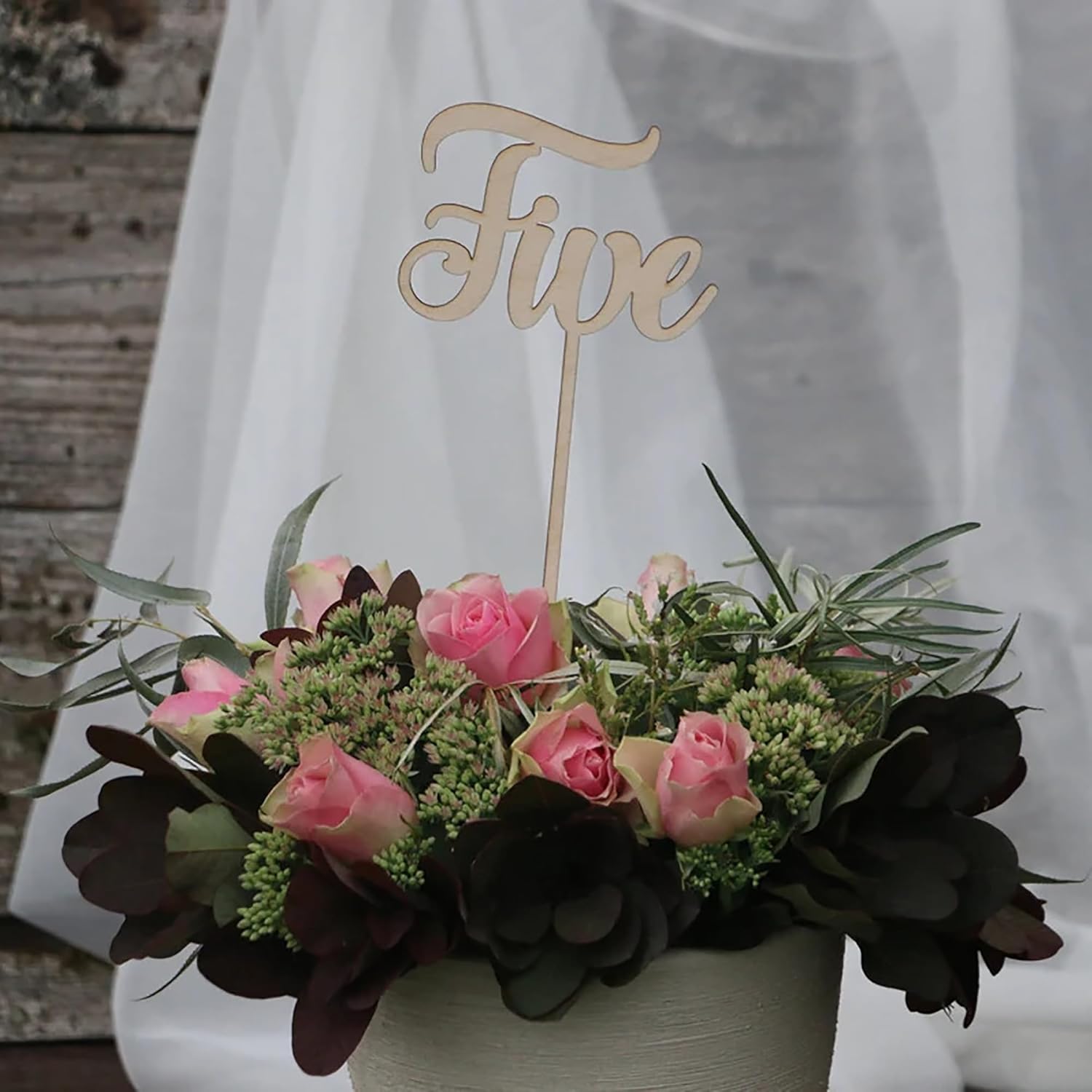 Floral arrangement with a 'Five' sign in the center against a white curtain background