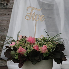 Floral arrangement with a 'Five' sign in the center against a white curtain background