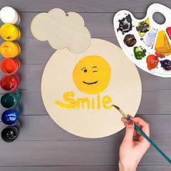 Painting a smiley face with the word 'Smile' on a wooden board, surrounded by paint bottles and a palette.