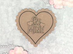 Heart-shaped cardboard cutout with 'Be Mine' text on a light background
