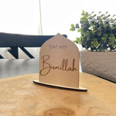 Wooden plaque with 'Start with Bismillah' text on a wooden surface with a blurred background