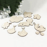 Set of wooden baby-themed decorations on a white surface with greenery in the background.