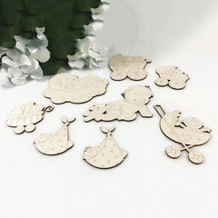 Set of wooden baby-themed decorations on a white surface with greenery in the background.