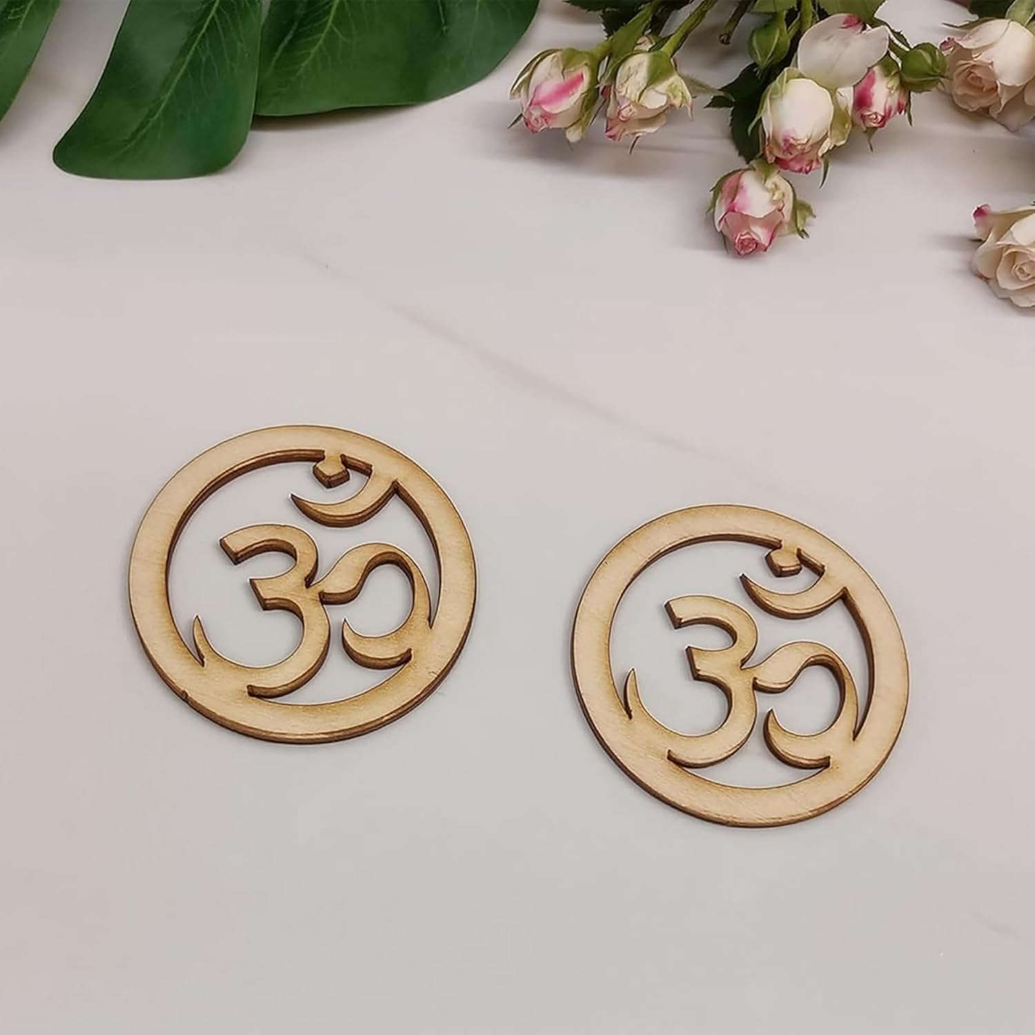 Two wooden OM symbol coasters on a light surface with flowers in the background