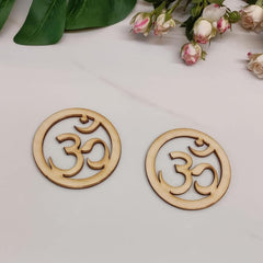 Two wooden OM symbol coasters on a light surface with flowers in the background