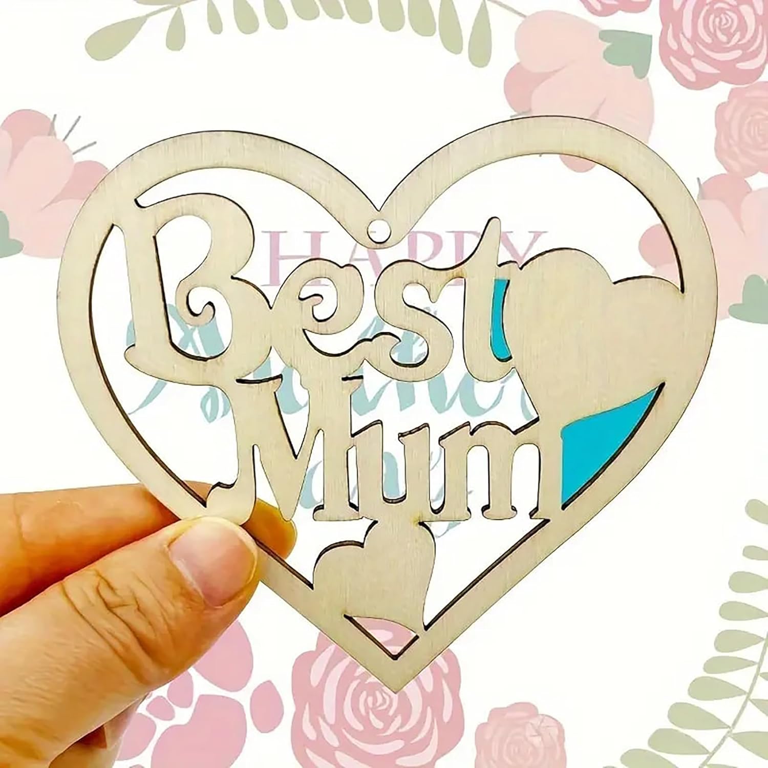 Heart-shaped wooden plaque with 'Best Mum' text held by a hand against a floral background.