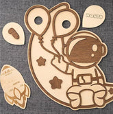Wooden astronaut-themed baby milestone board with attached cards on a gray fabric background