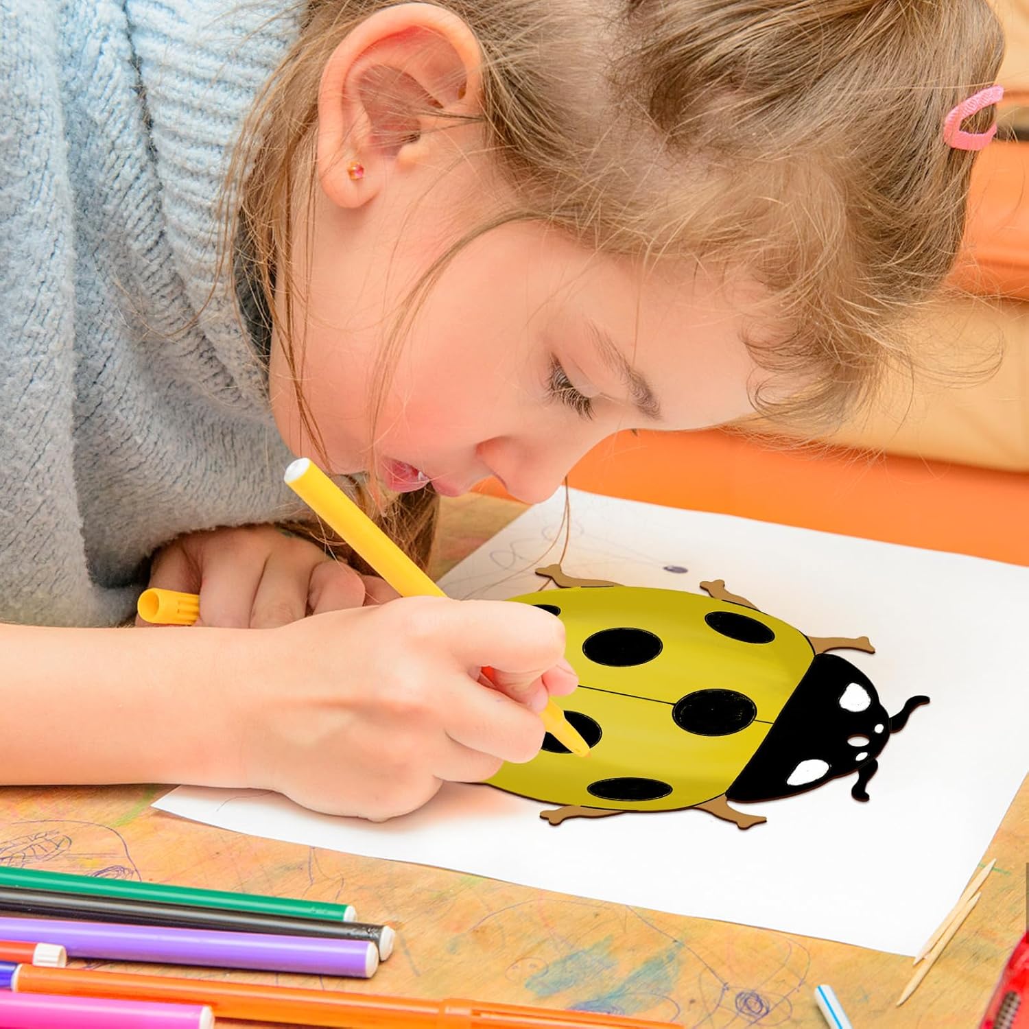 Child drawing a ladybug with colored pencils on a piece of paper.