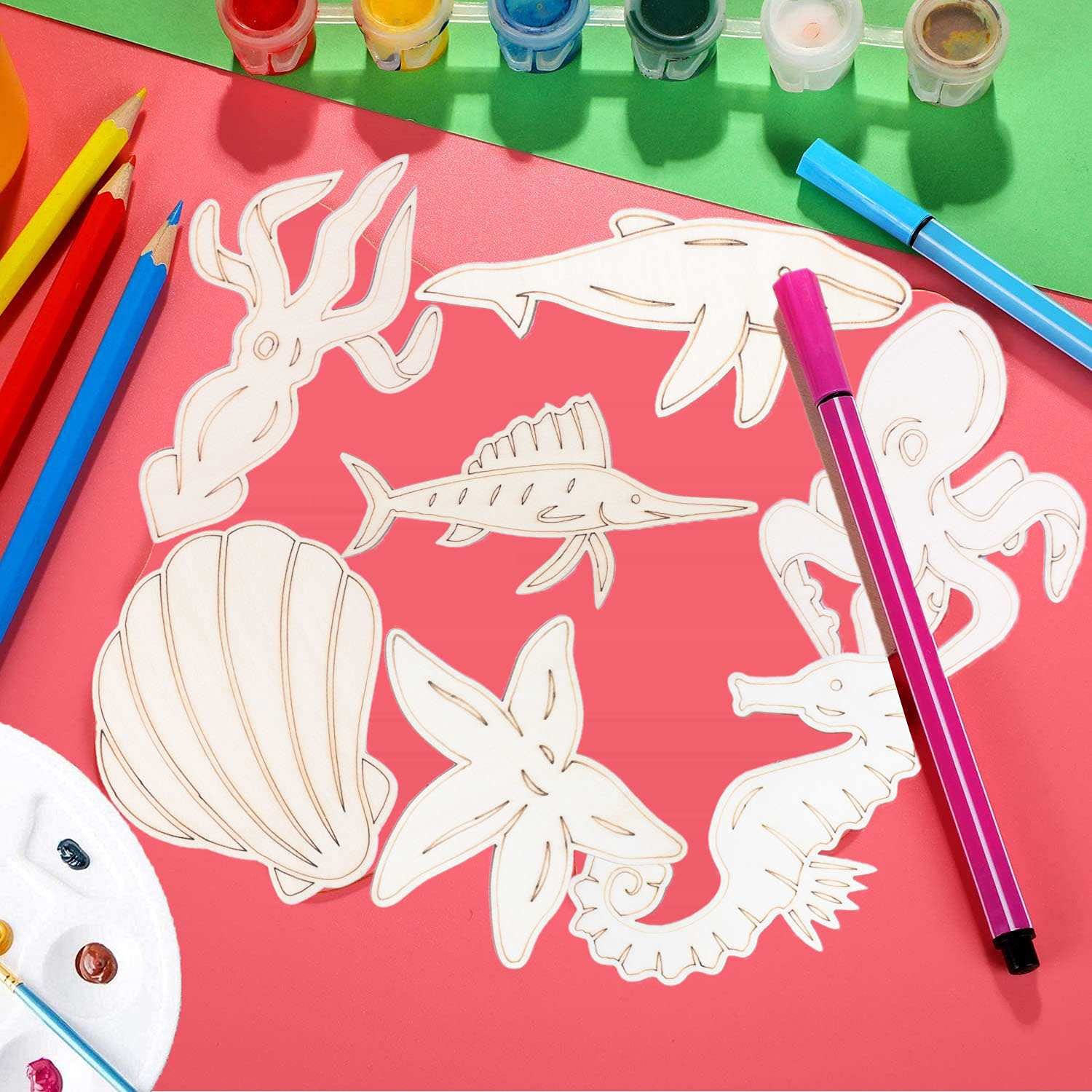 White cut-out sea creature shapes on a pink surface with art supplies including markers and paint.