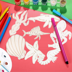 White cut-out sea creature shapes on a pink surface with art supplies including markers and paint.
