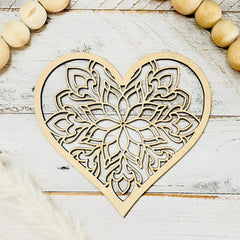 Wooden heart-shaped decorative item with intricate cut-out patterns on a light wooden surface.